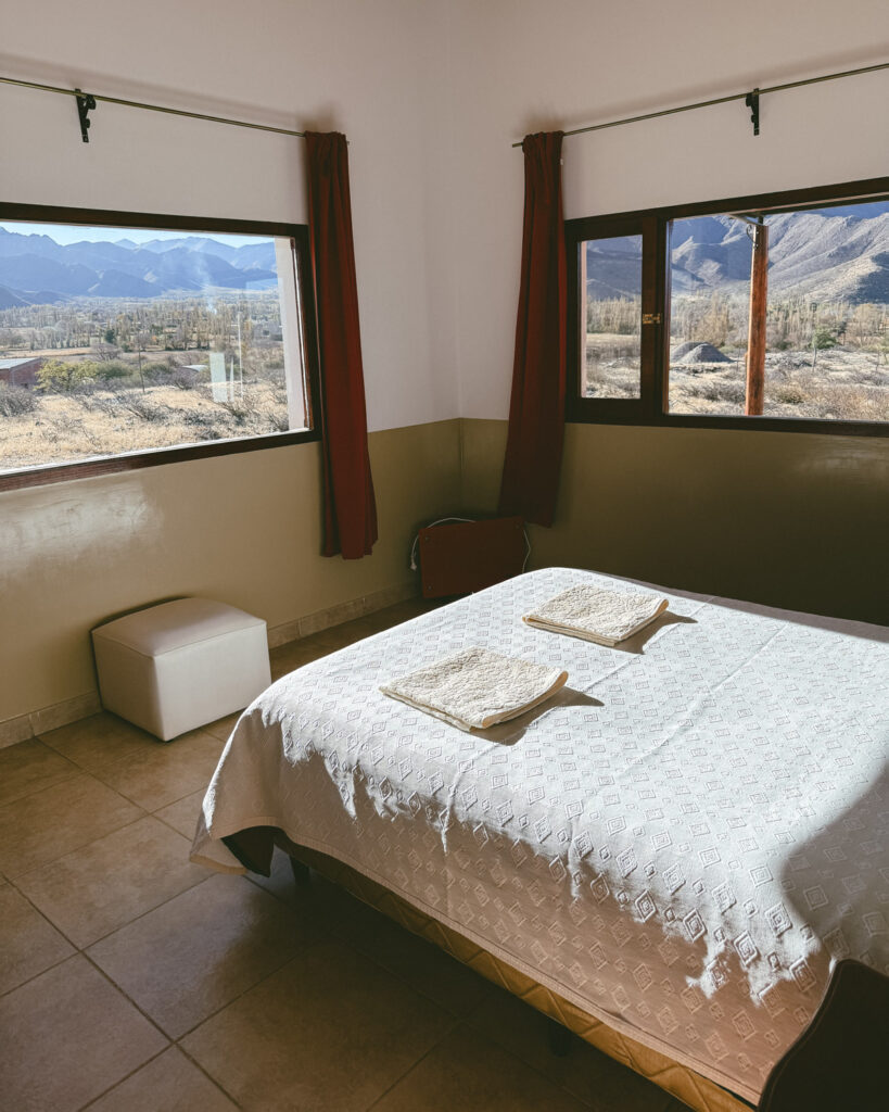7 - 10 Day Salta Road Trip: The Best of Northwest Argentina 58 A simple guest room with a double bed and white linens is brightly lit by two large windows offering panoramic mountain views in Cachi.