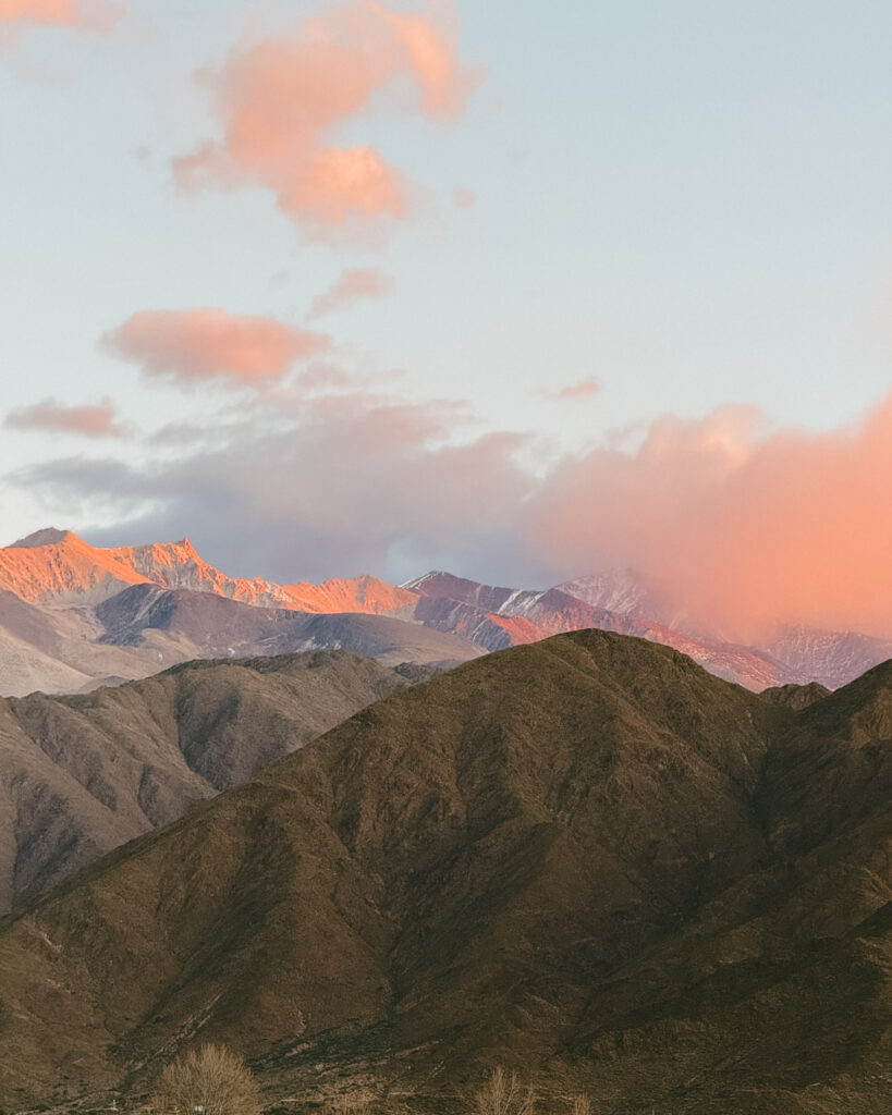 7 - 10 Day Salta Road Trip: The Best of Northwest Argentina 59 Snowy Andean peaks glowing with warm orange and pink hues at sunrise, partially shrouded by soft pastel clouds in the early morning sky.