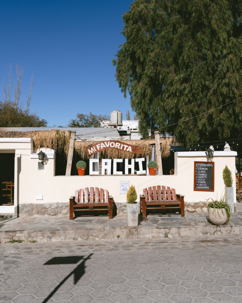7 - 10 Day Salta Road Trip: The Best of Northwest Argentina 56 Exterior of the restaurant “Mi Favorita” in Cachi, featuring a sign made of large white letters, wooden benches, and a chalkboard empanada menu.