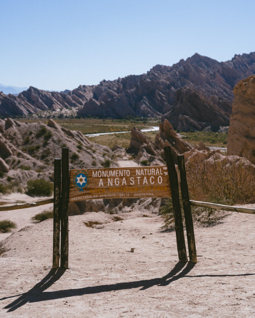 7 - 10 Day Salta Road Trip: The Best of Northwest Argentina 43 Sign for “Monumento Natural Angastaco Área Protegida Ley 6808” marks the protected area in Salta, Argentina, with sharp hills in the distance.