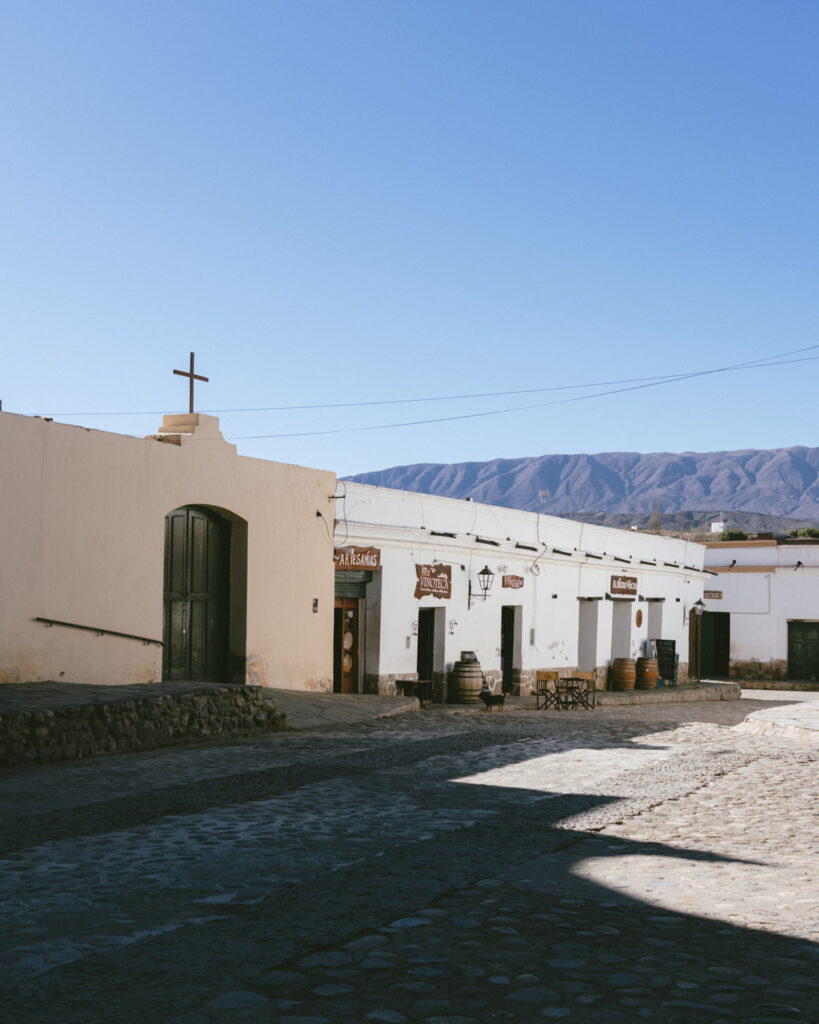 7 - 10 Day Salta Road Trip: The Best of Northwest Argentina 48 Corner view of a small white church with a cross and local artisan shops in a quiet cobblestone plaza in Cachi.