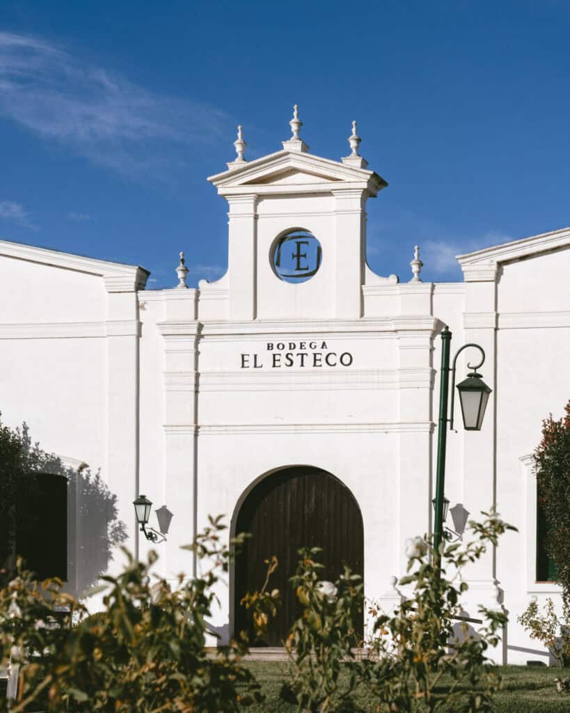 7 - 10 Day Salta Road Trip: The Best of Northwest Argentina 27 The entrance of El Esteco winery in Cafayate, Argentina, featuring classic white architecture with a central arched wooden door and a small clock tower above.