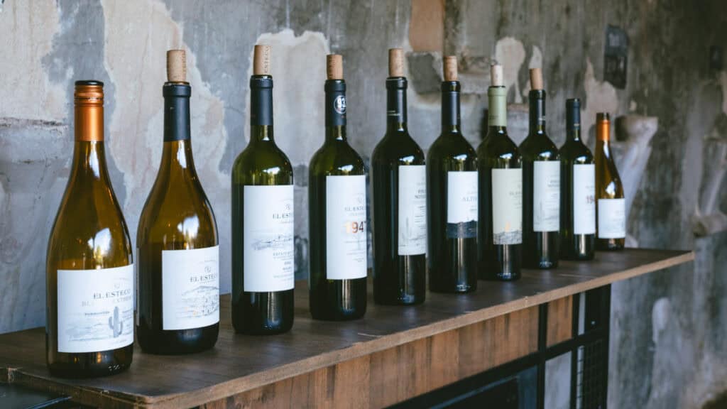 7 - 10 Day Salta Road Trip: The Best of Northwest Argentina 25 A lineup of El Esteco wine bottles, including Torrontés and Malbec varieties, displayed on a rustic wooden table against a weathered wall in Cafayate.