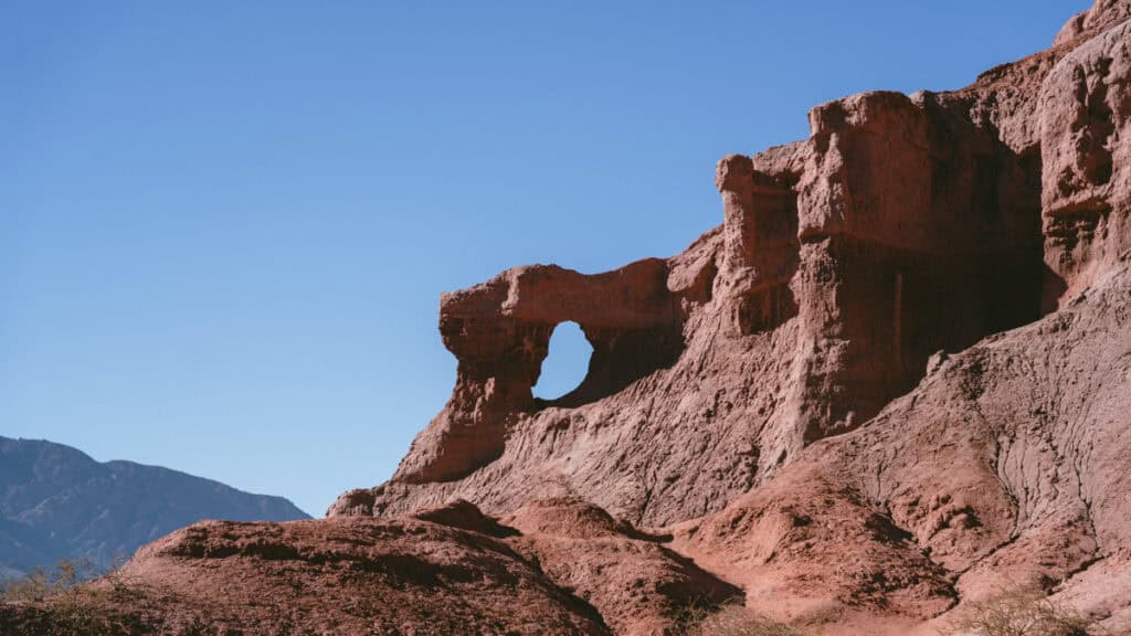7 - 10 Day Salta Road Trip: The Best of Northwest Argentina 24 A dramatic rock formation with a natural window-like hole stands against a bright blue sky in Quebrada de las Conchas.