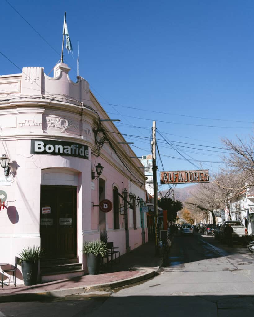 7 - 10 Day Salta Road Trip: The Best of Northwest Argentina 36 A corner café named Bonafide with pale pink walls and an Argentine flag stands on a sunny street, with a hanging “ALFAJORES” sign in the background.
