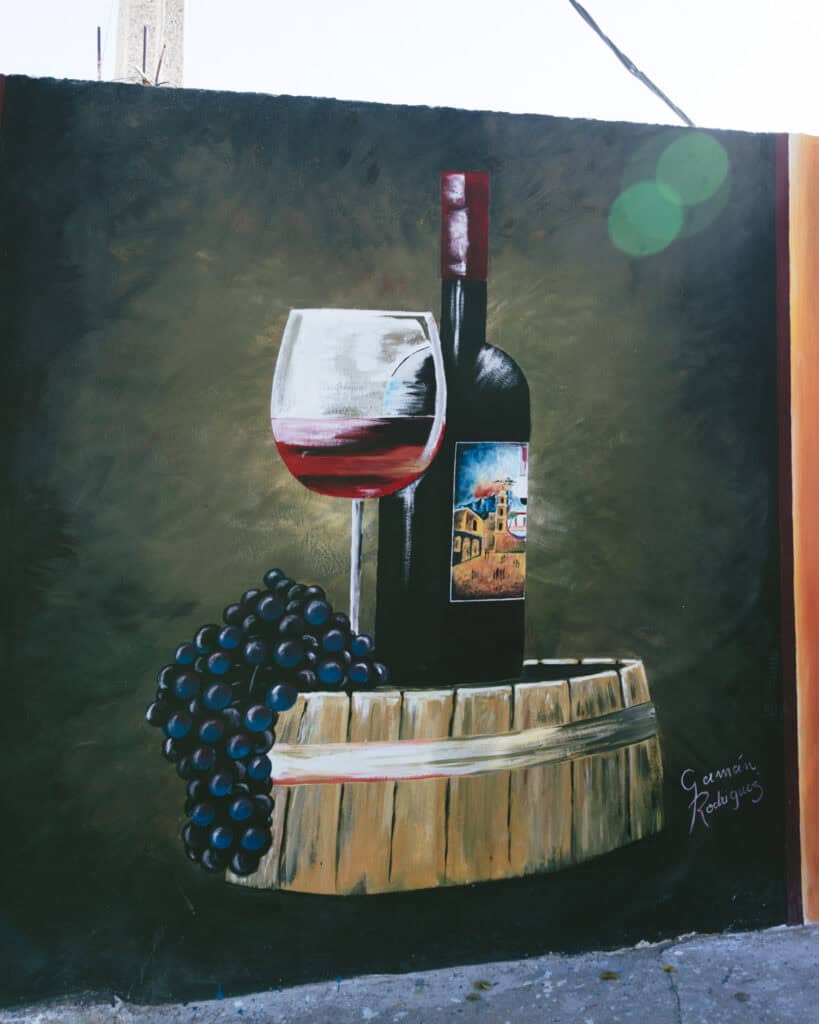 7 - 10 Day Salta Road Trip: The Best of Northwest Argentina 26 A detailed mural depicts a bottle and glass of red wine resting on a wooden barrel next to a bunch of grapes, painted on a dark green background.