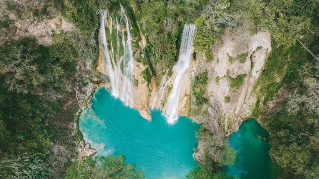 Huasteca Potosina: Guide to Mexico's Waterfall Wonderland 1 Aerial view of Cascadas Minas Viejas in Huasteca Potosina, where multiple waterfalls cascade down mossy limestone cliffs into two stunning turquoise pools. The falls are surrounded by dense forest and steep rock formations.