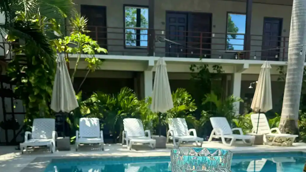 Where to Stay in El Tunco: 16 Best Options for Every Budget 8 The pool at Dos Palmas Hostel in El Tunco, with sun loungers lined up with white umbrellas.