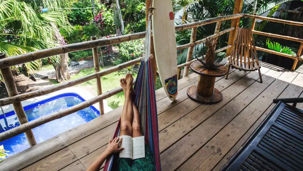 Where to Stay in El Tunco: 16 Best Options for Every Budget 9 Eco del Mar hotel in El Tunco, with a set of anonymous legs lazing on a hammock on a deck overlooking the pool. The person is reading a book.