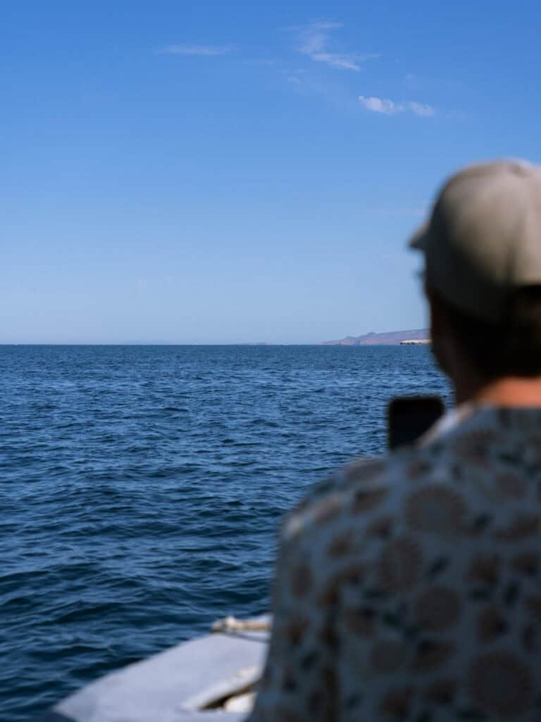 Our Day at Isla Espiritu Santo, La Paz: Sea Lions & Beaches 12 Brayden sits at the front of a boat looking out over the open sea toward the distant coastline of Isla Espiritu Santo in La Paz Baja California Sur under a clear blue sky.