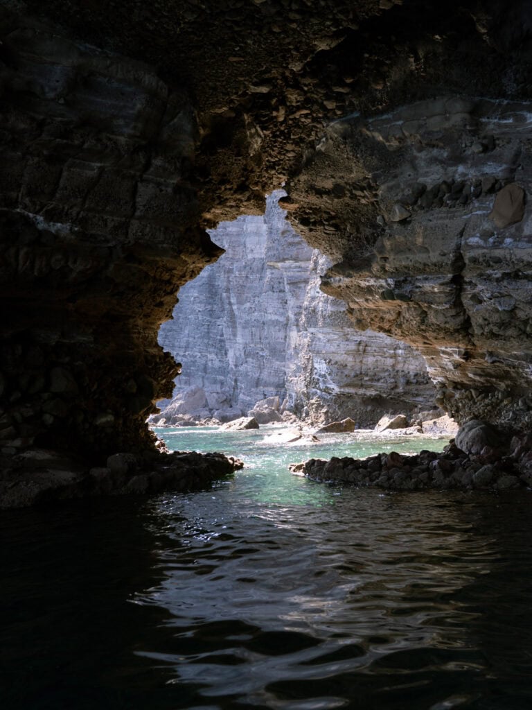 Our Day at Isla Espiritu Santo, La Paz: Sea Lions & Beaches 19 Interior of a rocky sea cave with textured stone walls opening to bright turquoise water and sunlit cliffs outside on Isla Espiritu Santo in La Paz Baja California Sur.