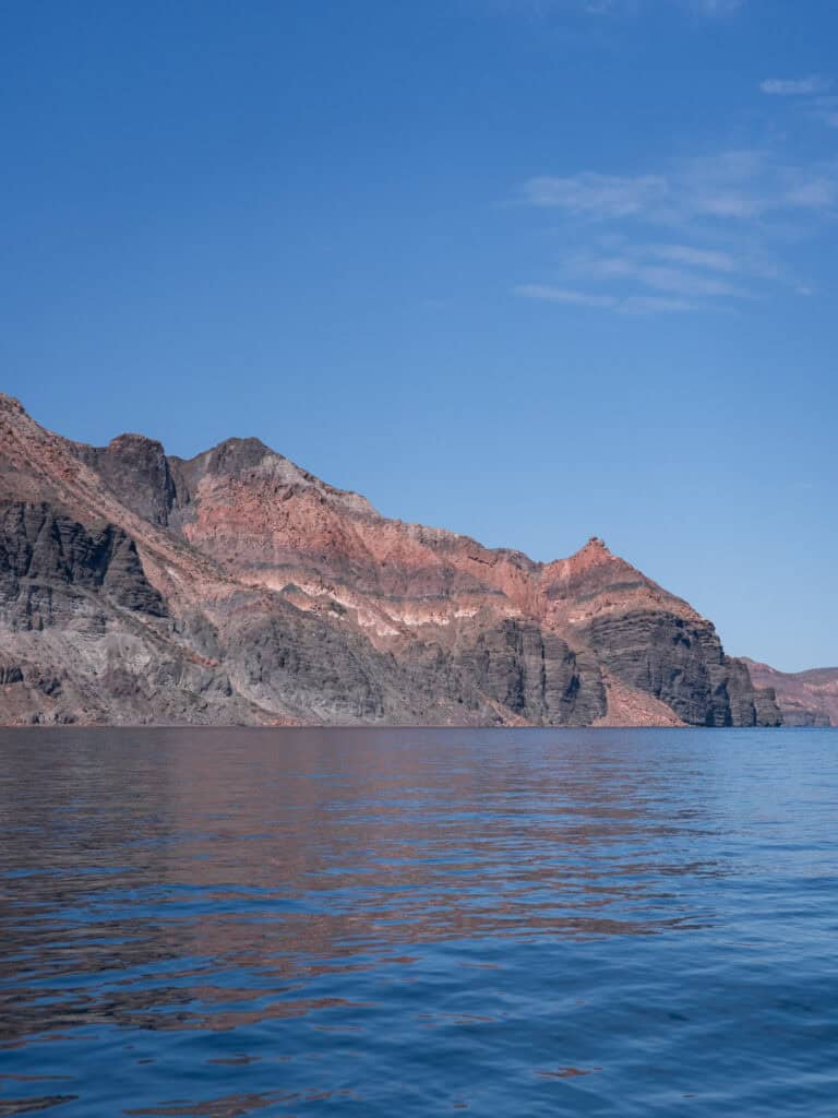 La Paz Mexico Travel Guide: Baja's Underrated Capital 19 Low rocky hills stretch across the horizon beyond calm ocean water at Isla Espiritu Santo in La Paz Baja California Sur on a bright sunny day.