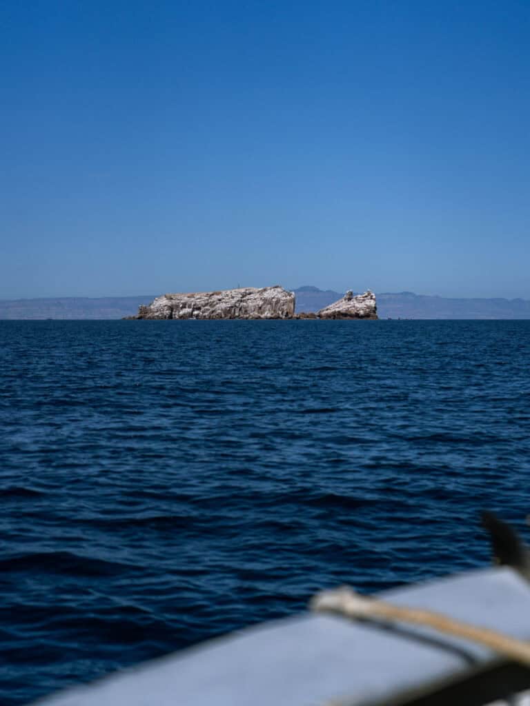 Our Day at Isla Espiritu Santo, La Paz: Sea Lions & Beaches 22 A small rocky island sits in the distance surrounded by deep blue ocean with hazy mountains on the horizon near Isla Espiritu Santo in La Paz Baja California Sur.