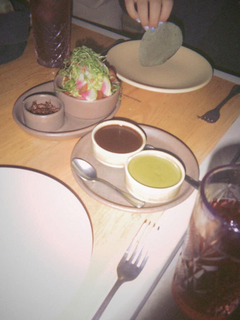 Mexico City Food Tour: Our Experience with Sherpa Food Tours 22 A restaurant table in Mexico City holds small bowls of dark and green sauces alongside a colorful dish topped with sliced vegetables as a hand reaches in holding a tortilla.