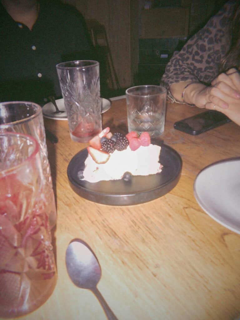 Mexico City Food Tour: Our Experience with Sherpa Food Tours 20 A dessert topped with strawberries and blackberries sits on a plate in a dimly lit Mexico City restaurant surrounded by glasses and two diners seated at the table.
