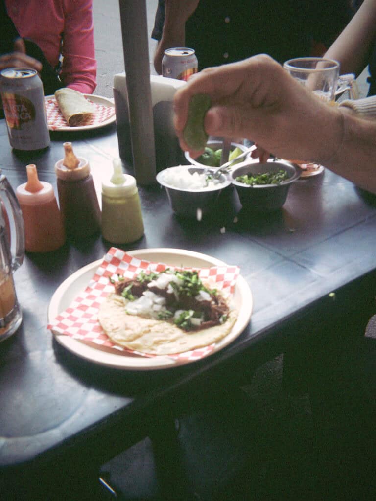 Mexico City Food Tour: Our Experience with Sherpa Food Tours 3 A hand squeezes fresh lime over a taco topped with chopped onions and cilantro on a plate surrounded by salsas, drinks, and other diners during a Mexico City food tour.