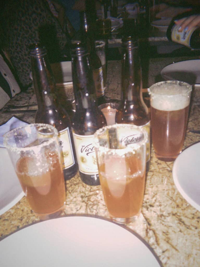 Mexico City Food Tour: Our Experience with Sherpa Food Tours 18 Several glasses with salted rims filled with a light brown drink sit on a table alongside empty beer bottles and plates in a dimly lit Mexico City restaurant during a food tour.