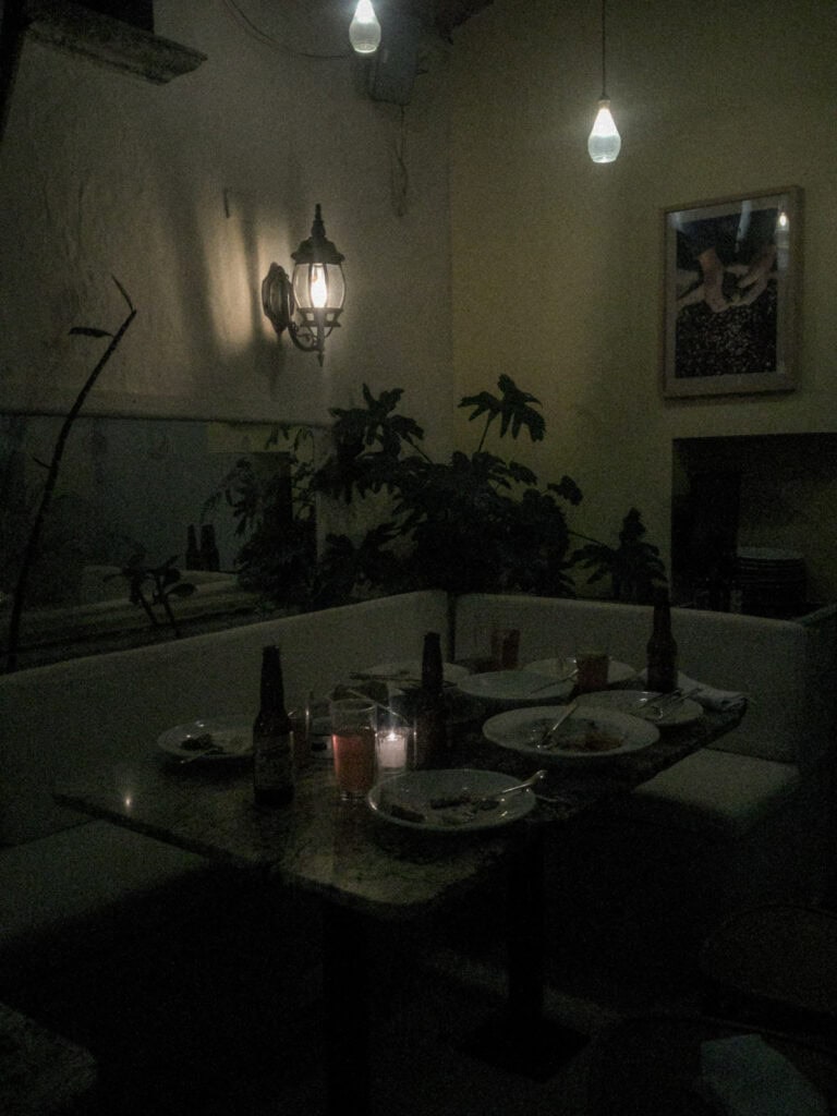 Mexico City Food Tour: Our Experience with Sherpa Food Tours 23 A dimly lit restaurant interior in Mexico City shows a table set with plates, candles, and drinks surrounded by plants and warm hanging lights during a food tour.