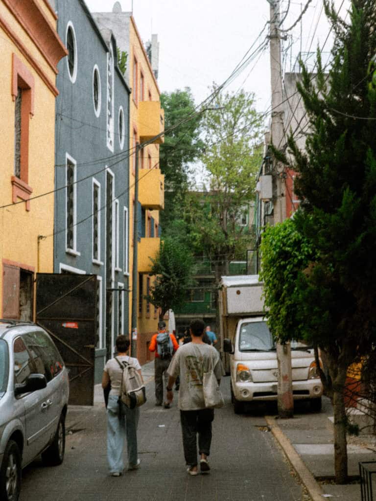 Mexico City Food Tour: Our Experience with Sherpa Food Tours 4 Group walking down a narrow street in Mexico City lined with colorful buildings, parked cars, and overhead wires during a food tour.