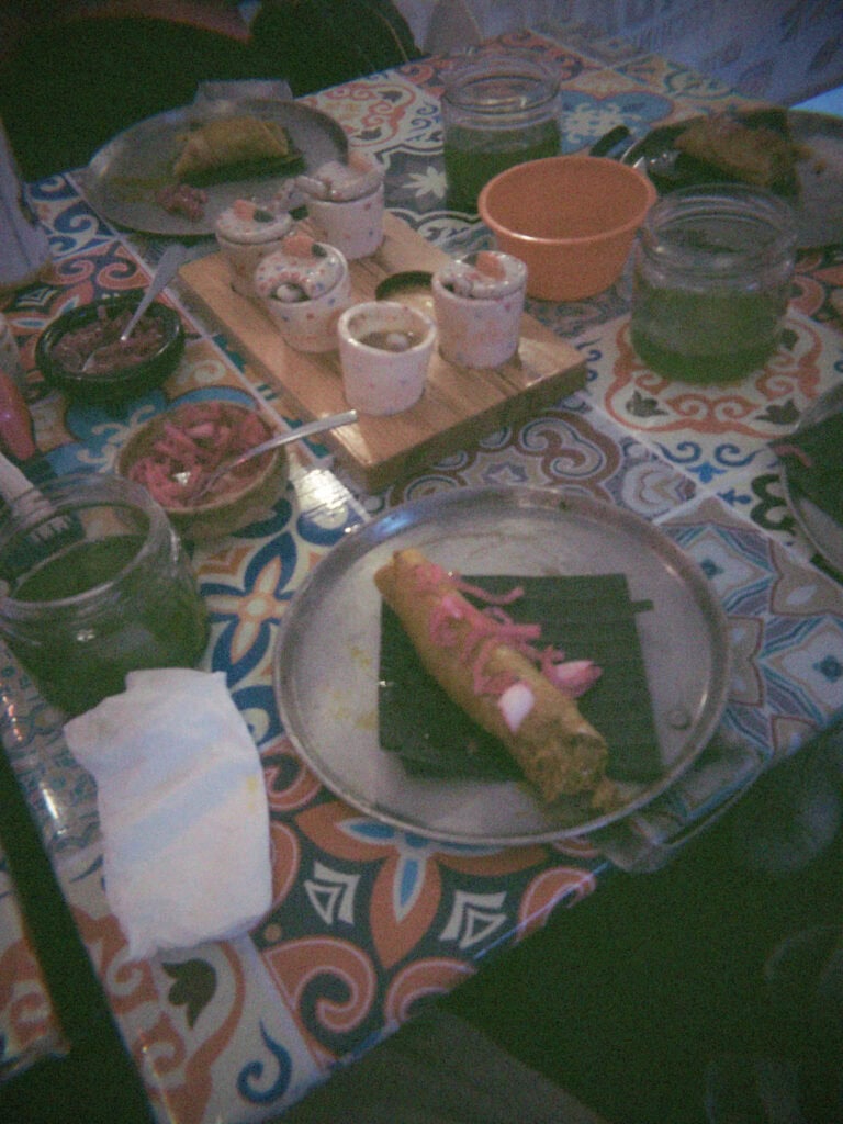 Mexico City Food Tour: Our Experience with Sherpa Food Tours 5 A rolled taco topped with pickled onions sits on a metal plate beside bowls of salsa and condiments on a vibrant tiled table during a Mexico City food tour.