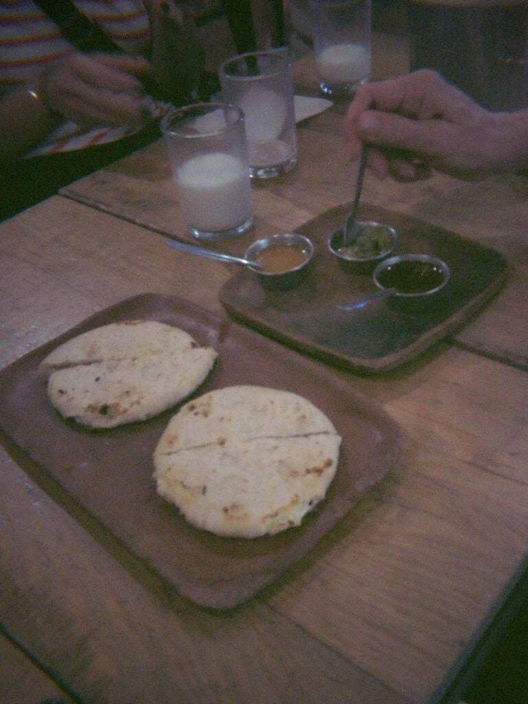Mexico City Food Tour: Our Experience with Sherpa Food Tours 16 A plate of thick corn tortillas sits on a wooden table next to small bowls of sauces while diners reach in to taste them during a Mexico City food tour.